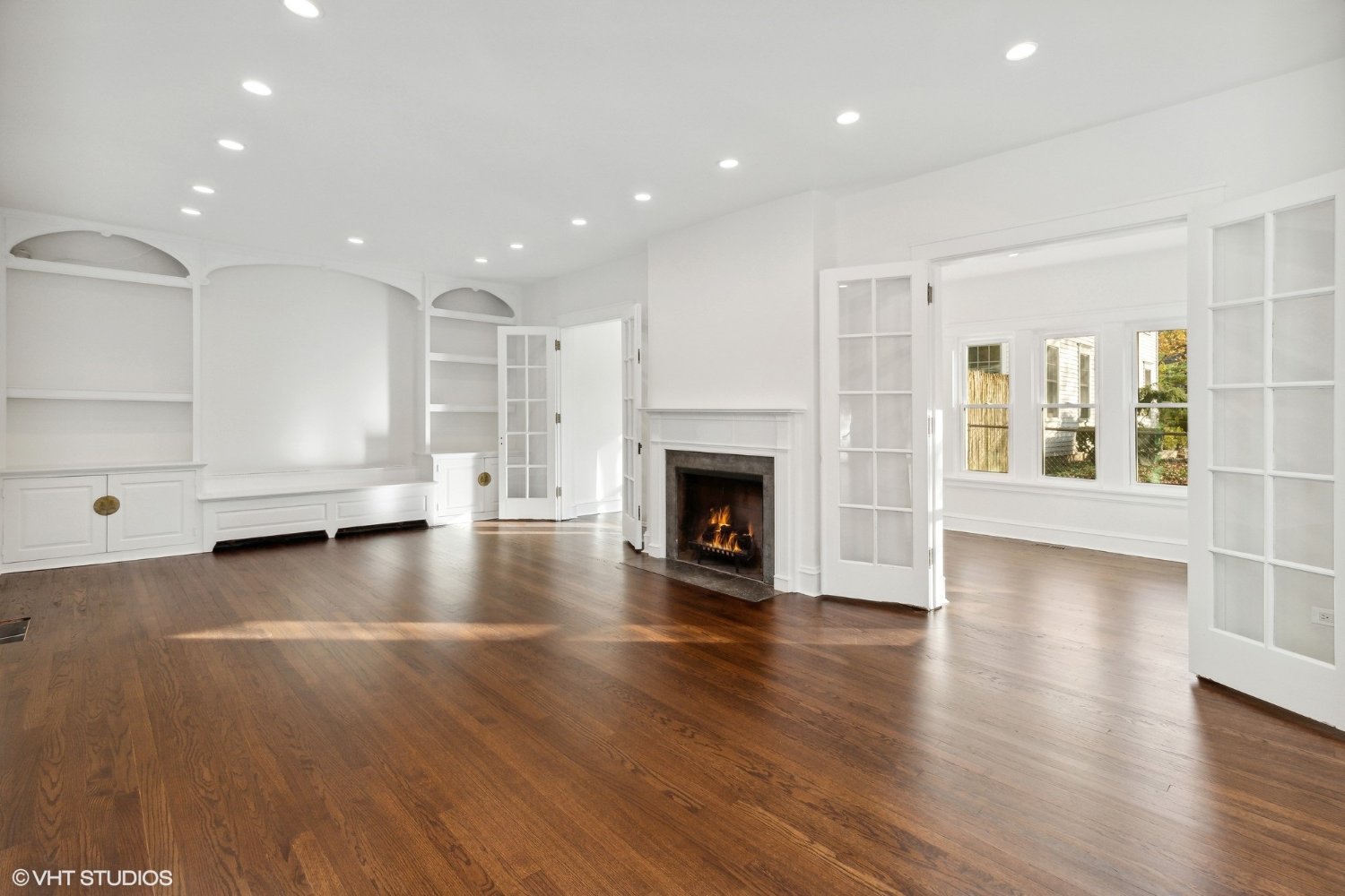 Empty living room with grand fireplace, built-in bookcases, and sun room view in a renovated Lake Forest single family home. This is a before photo, demonstrating the dramatic impact of professional home staging.