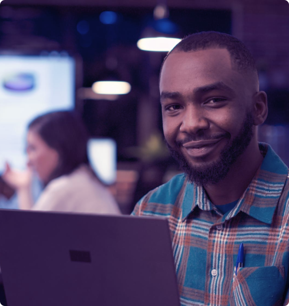 Foto de um desenvolvedor em seu computador, sorrindo, olhando em direção à câmera.