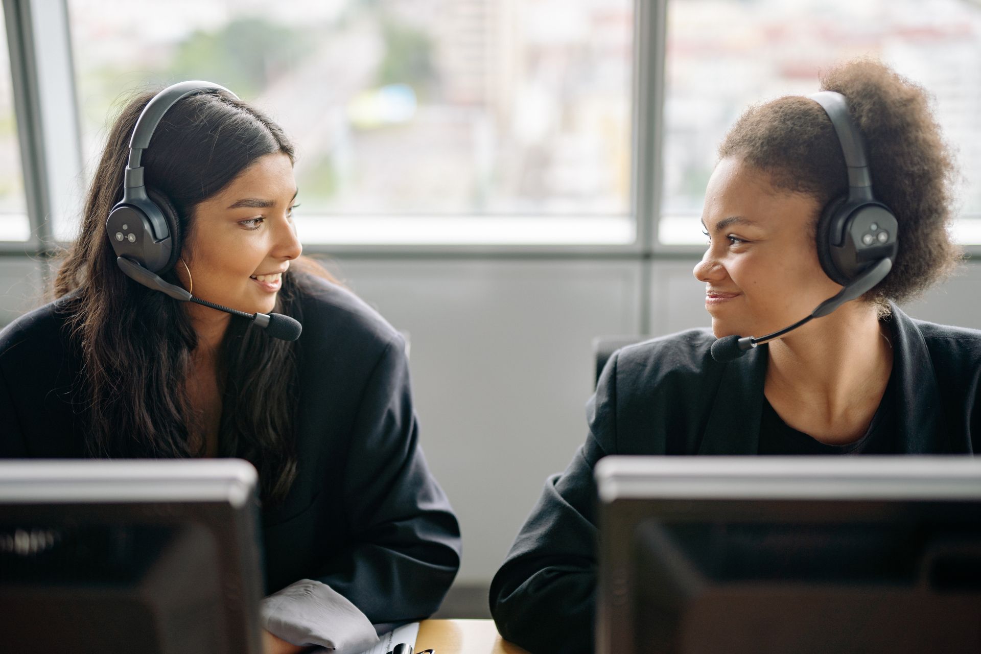 Two customer service representatives wearing headsets talking to each other at their desks