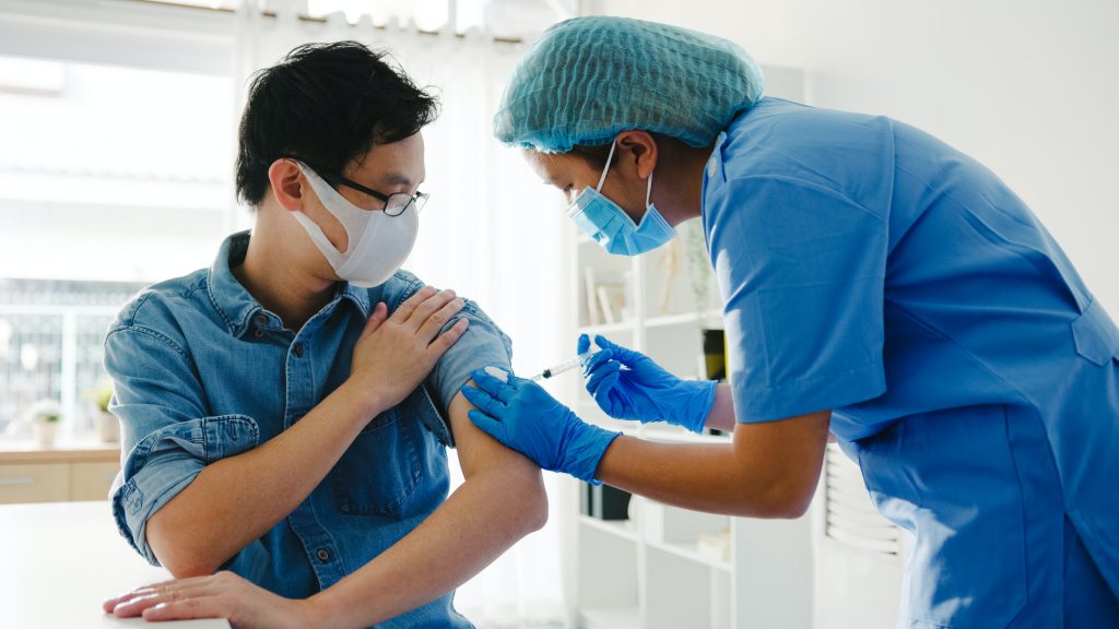 Young lady nurse giving Covid-19 or flu antivirus vaccine shot to senior male patient at hospital.