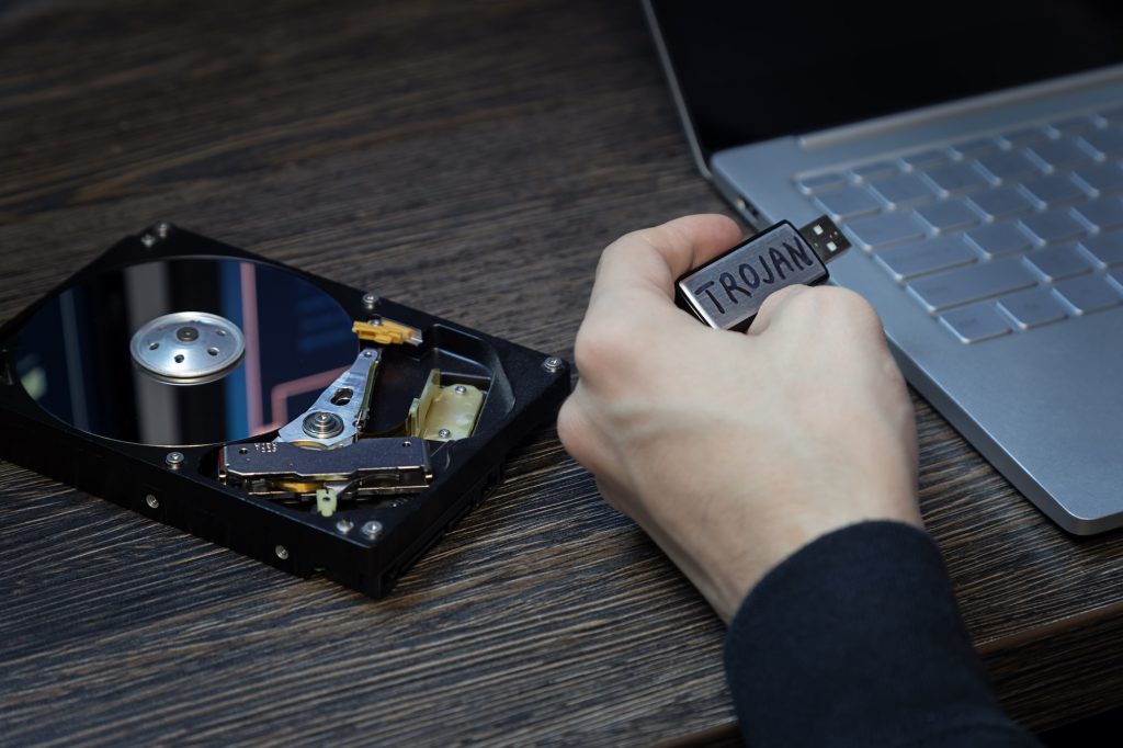 Man's hand with a flash drive infected with a virus and an open laptop on the desk