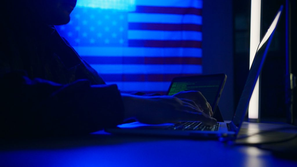 Hacker with laptop and USA flag in background. Cyber attack concept