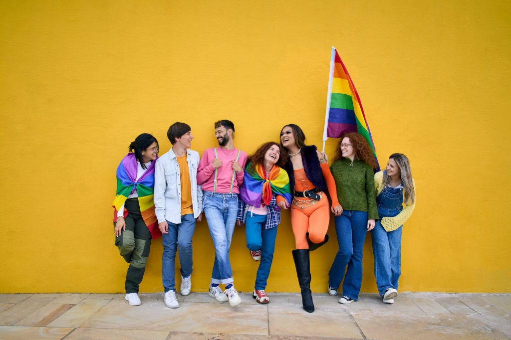 Portrait cheerful young group of friends standing on wall yellow. LGBT community smiling people.