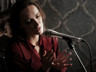 A female vocalist in a red blouse singing into the Shure KSM8 Microphone with a grey background 