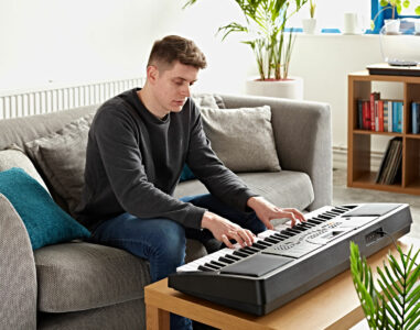 Man sat on sofa in living room playing the MK-4000 61-Key Keyboard by Gear4music