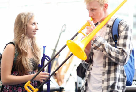 Two teenagers with pInstruments - a boy with a yellow pBone and a girl with a blue pTrumpet 