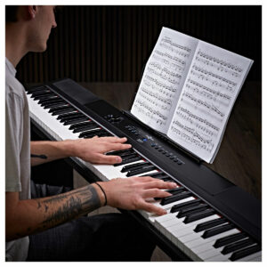 Man playing the black SDP-2 Stage Piano by Gear4music with sheet music in a dark studio