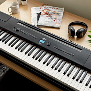 Black SDP-3 Stage Piano by Gear4music on a desk with headphones, mugs, magazines, and plants surrounding 