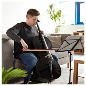 Man sat on the sofa playing cello whilst reading sheet music 