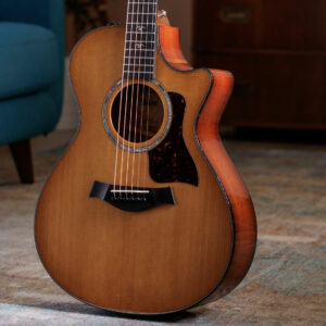 The body of the Taylor 512ce electro acoustic guitar with a blue sofa in the background