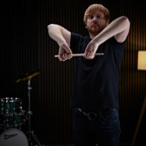 A drummer bending his arms whilst holding a drumstick, ensuring a deep stretch before drumming