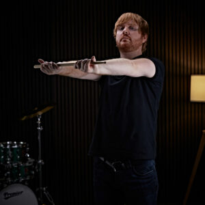 A drummer stretching out his arms whilst holding a drumstick