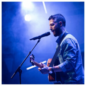 A man singing on stage with a guitar, using a Sennheiser wireless system