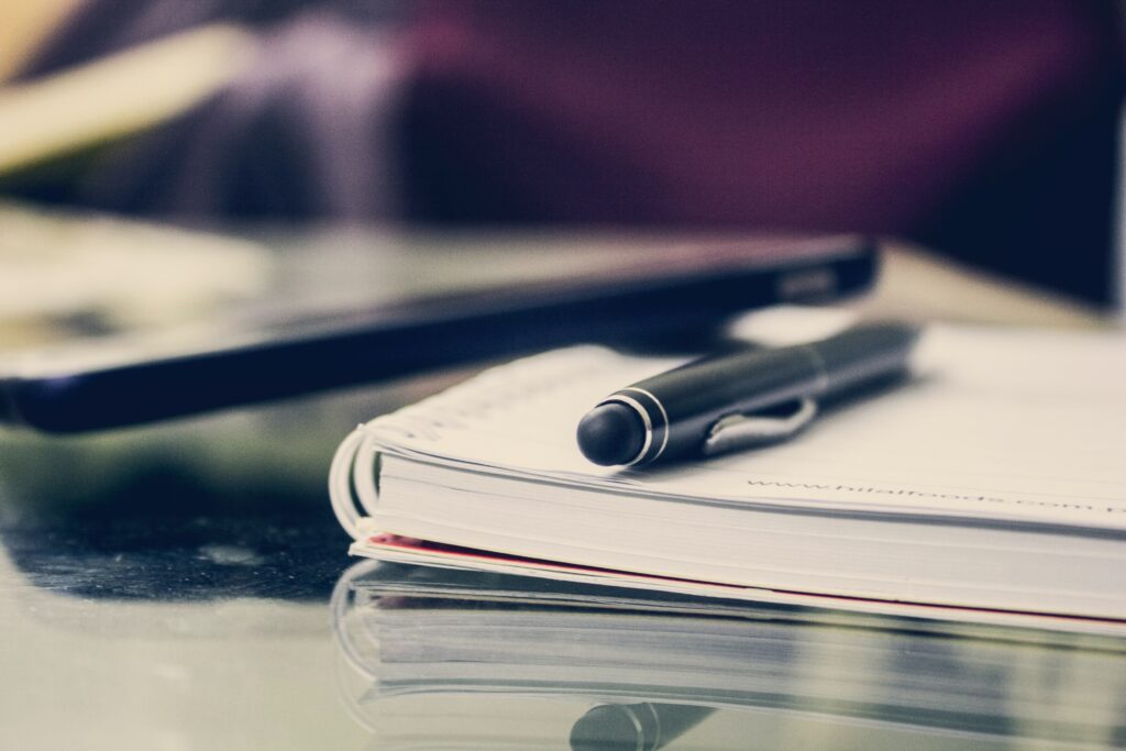 Close up of a pen sitting on top of a notebook on a glass desk.