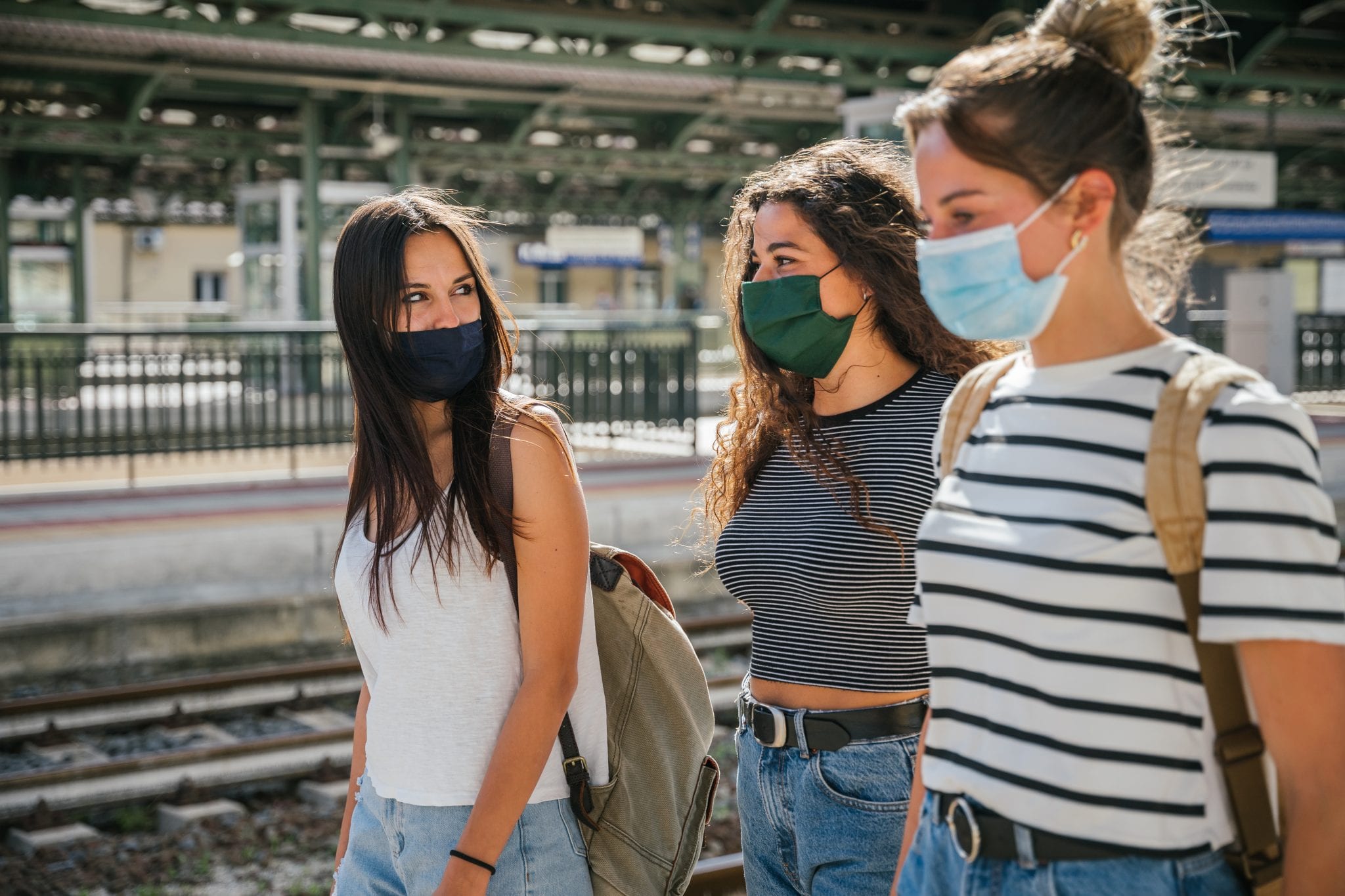 Three young friends women at the station walking and waiting train for their trip in summer with face mask for protection by infection from Corona virus, Covid-19 - Millennials having fun together