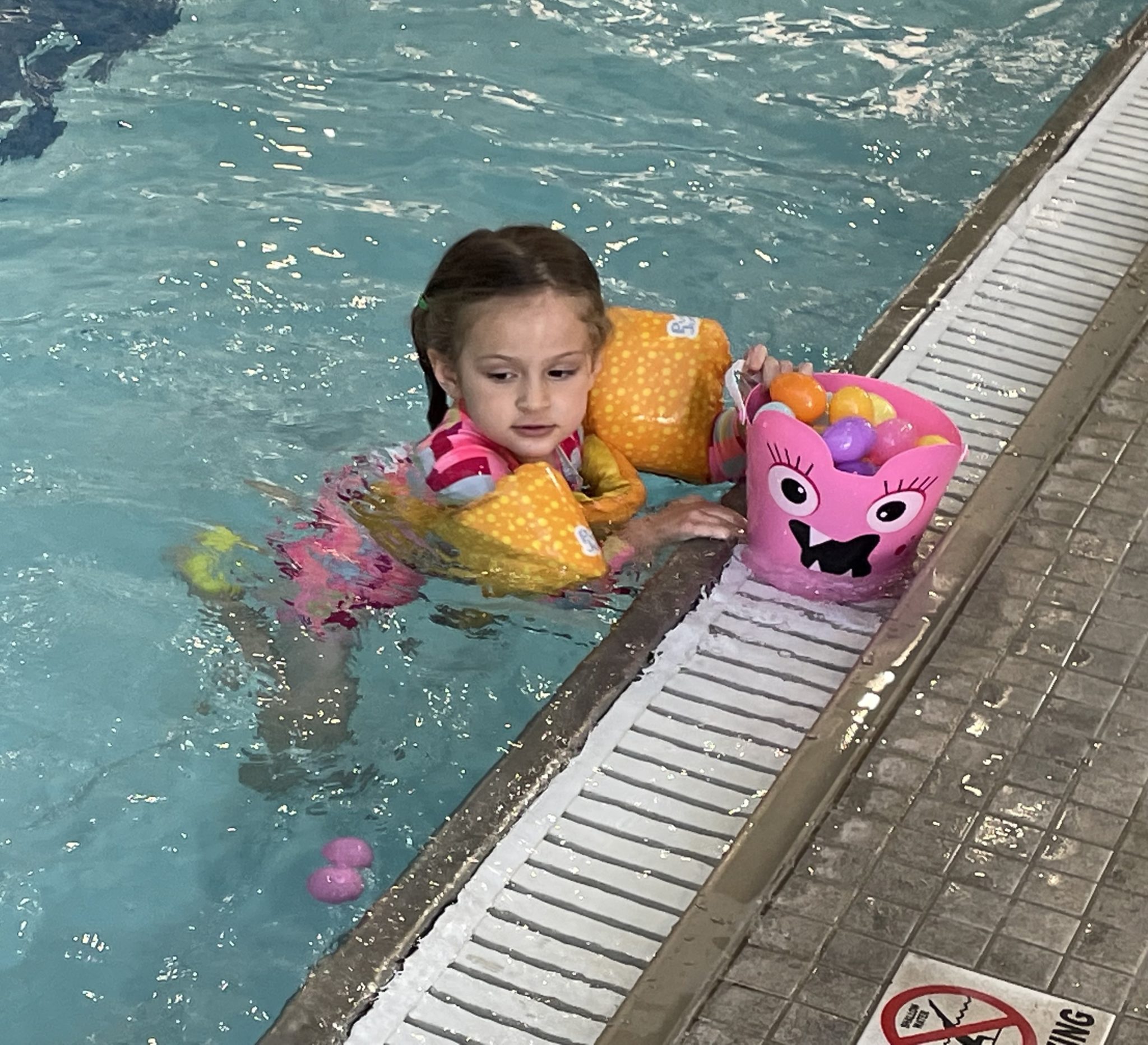 little girl rests at side of pool with basket of Easter eggs