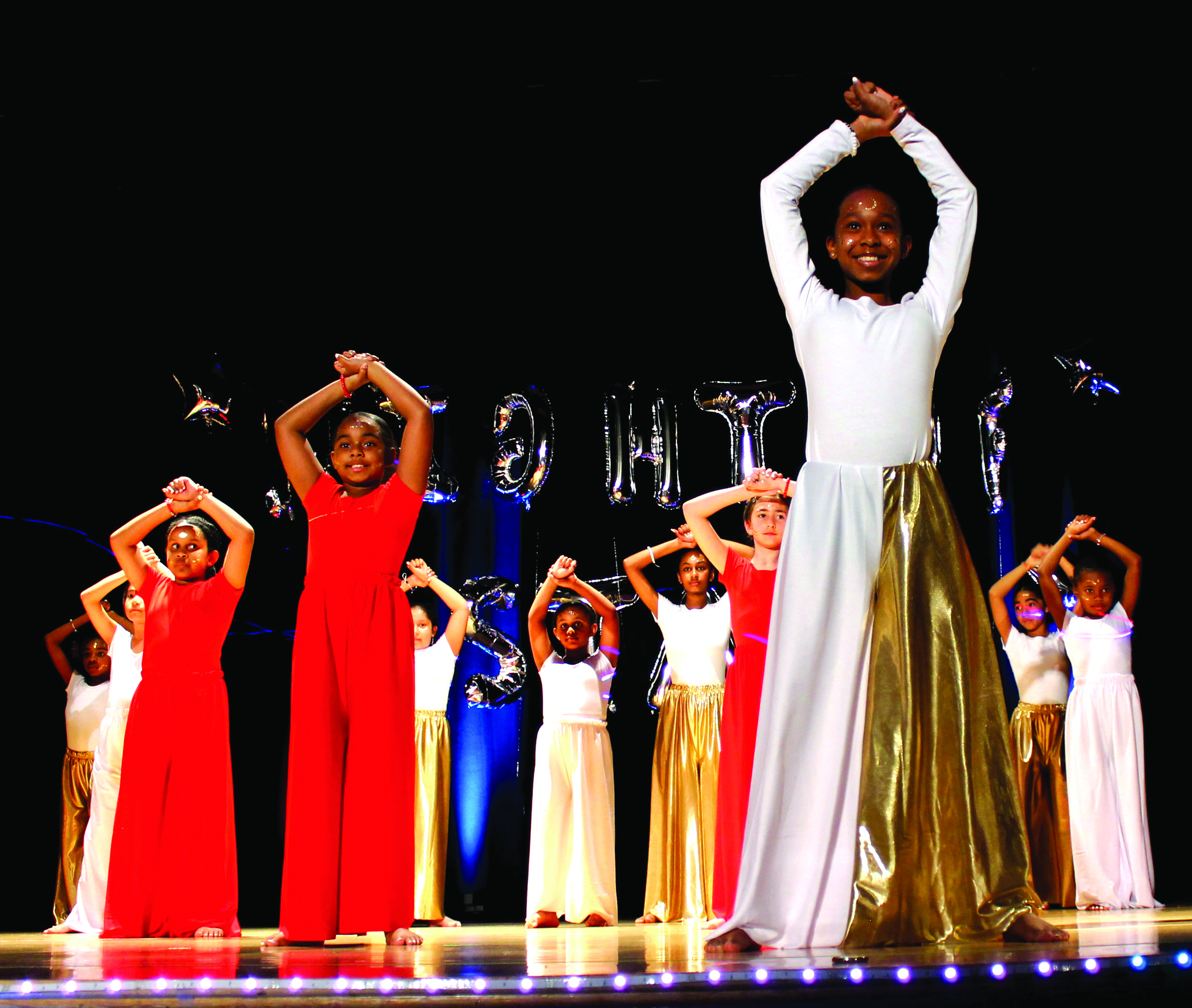 group of youth students performs in multi-colored outfits on stage