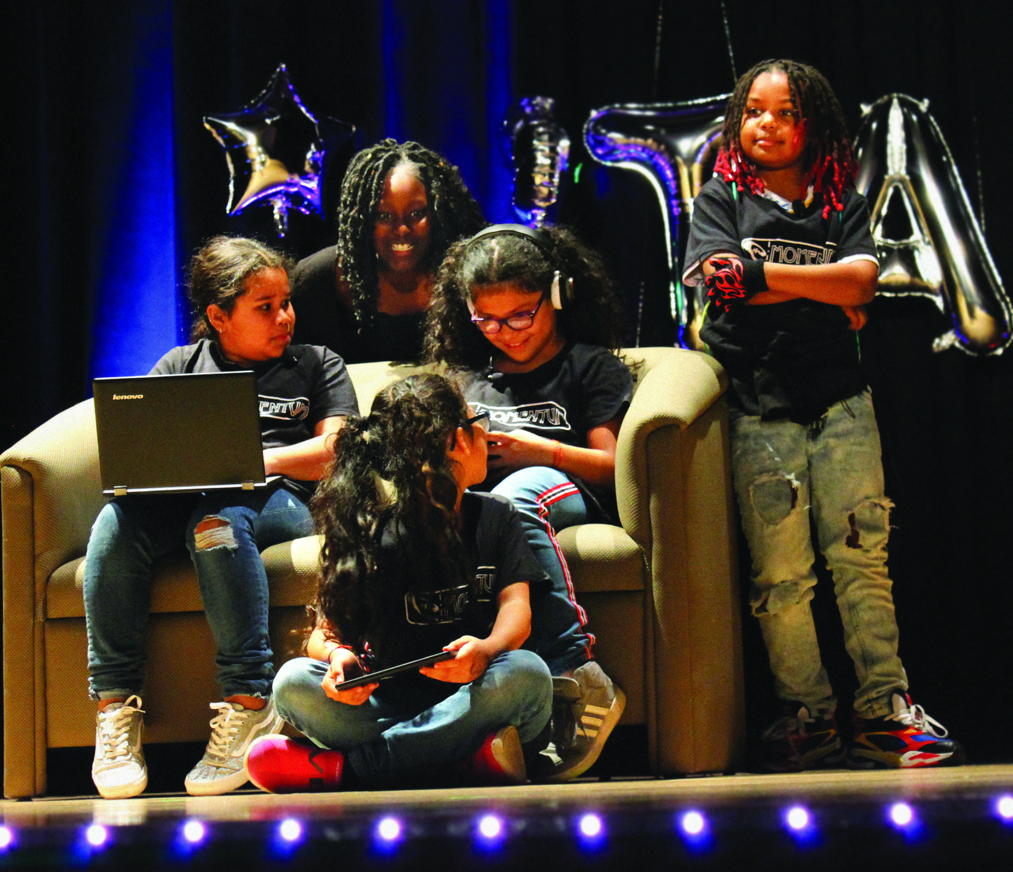 group of students performs scene on stage with couch and laptop as props