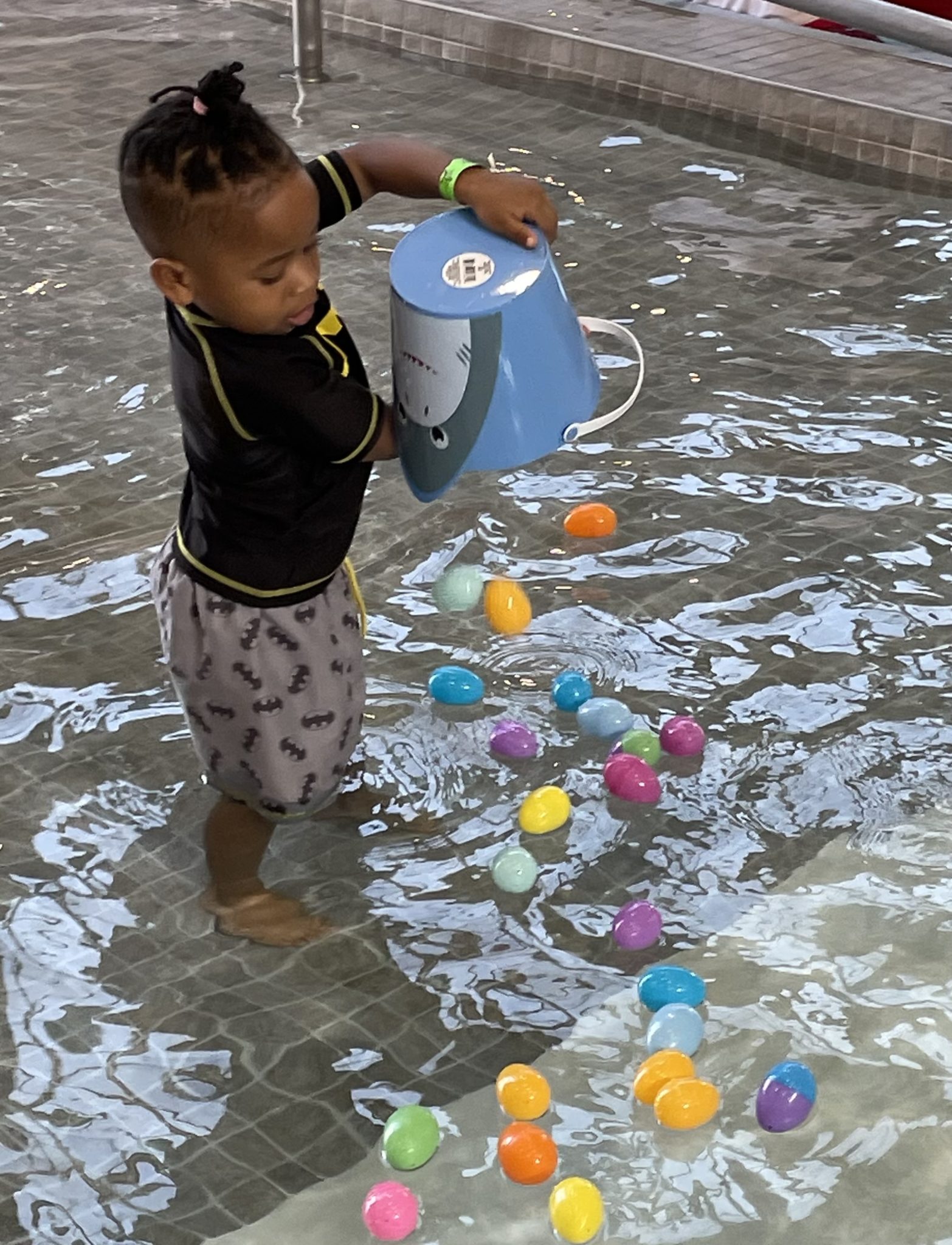 little boy standing in shallow pool tipping over his Easter basket