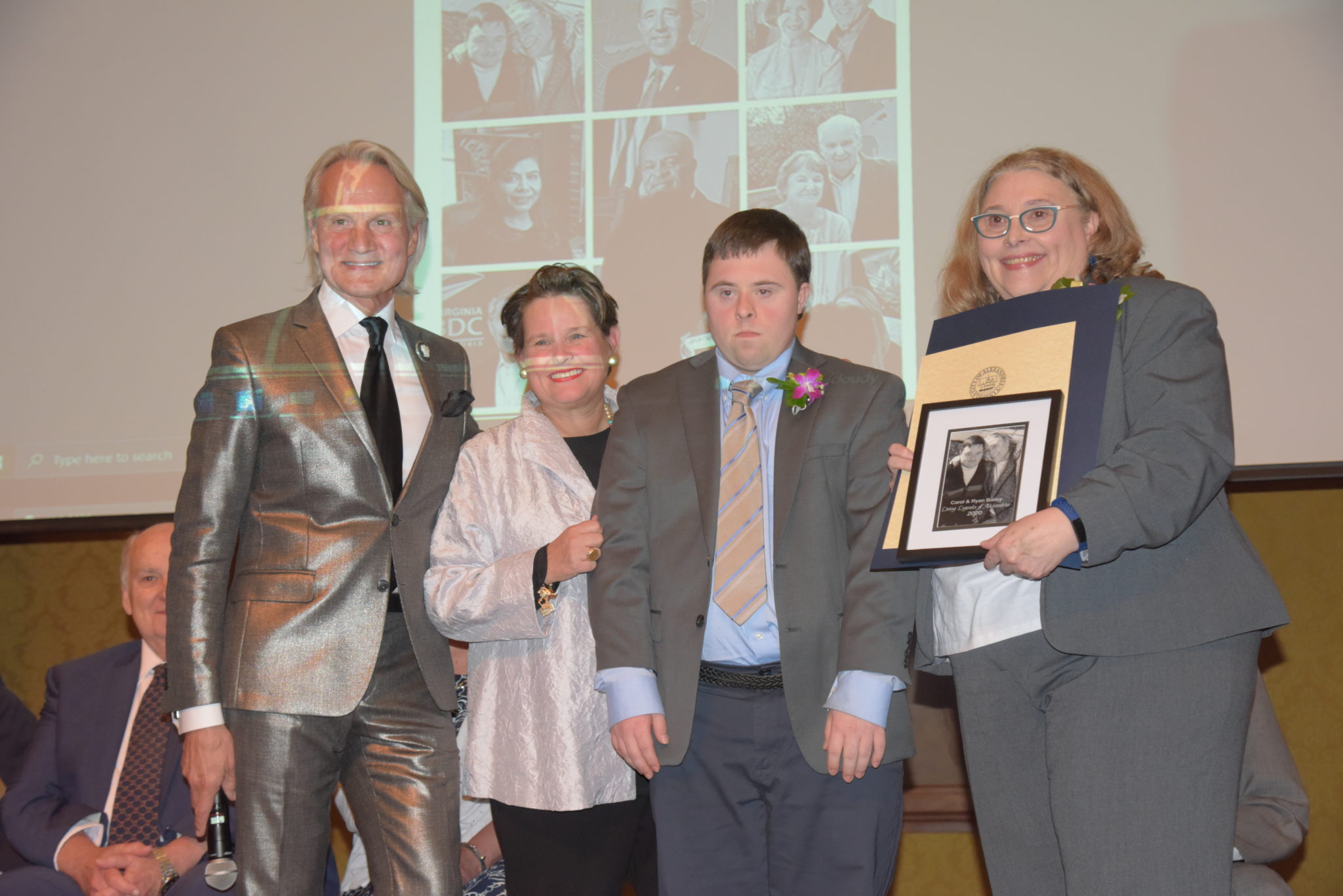 Monte Durham, Mary Wadland, Ryan and Carol Bailey, stand on stage holding photos and certificates