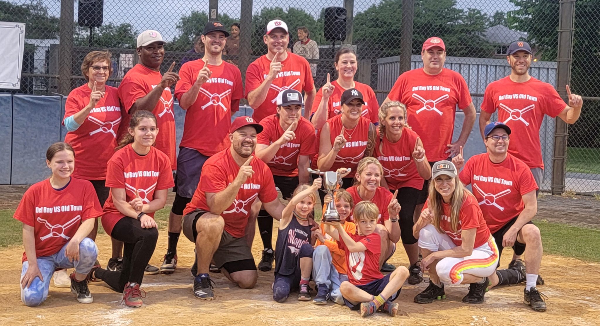 the del ray business association standing in a group on a baseball field after they won the john porter cup in the annual old town del ray softball game