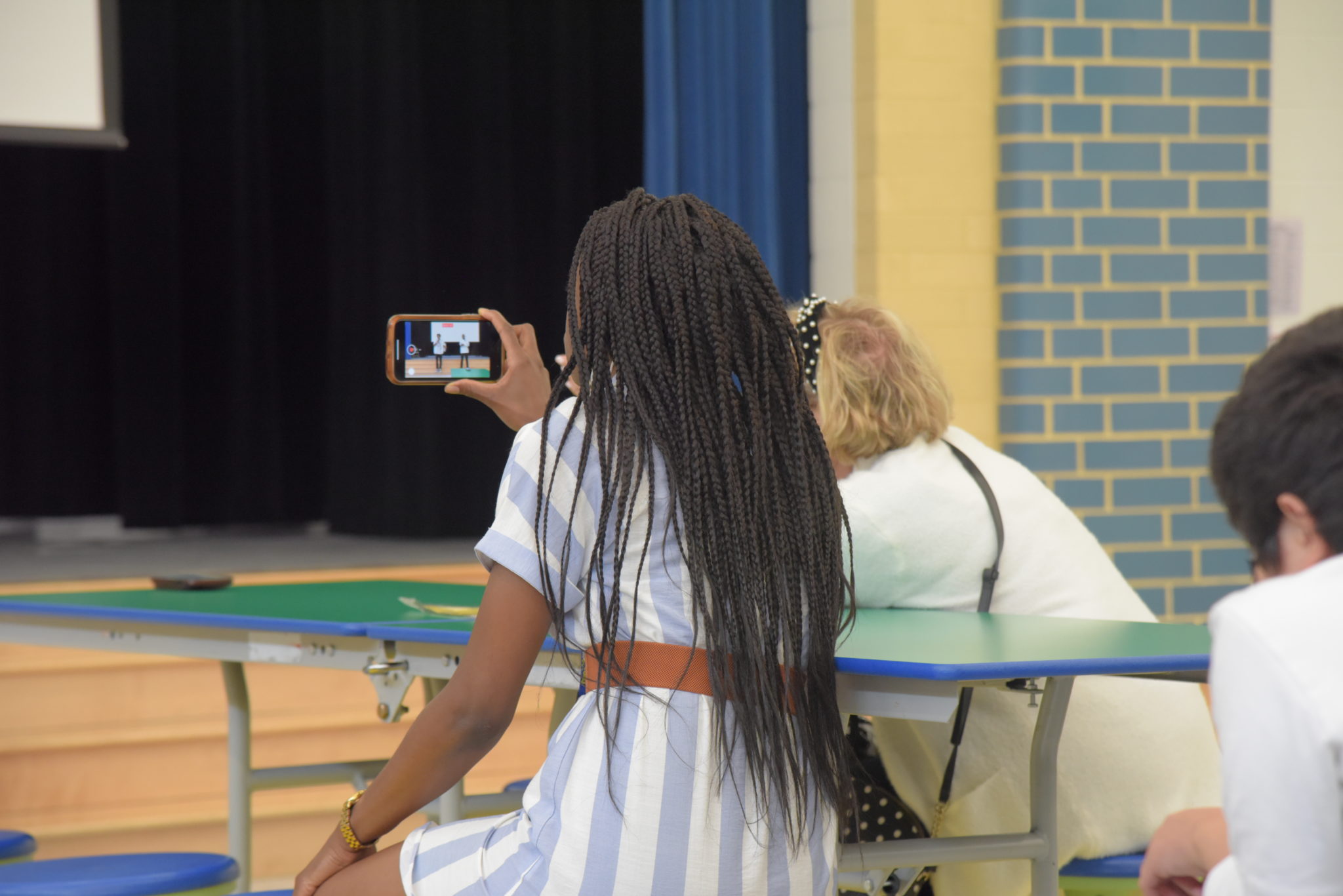 a woman sits at a table taking a video on her phone 