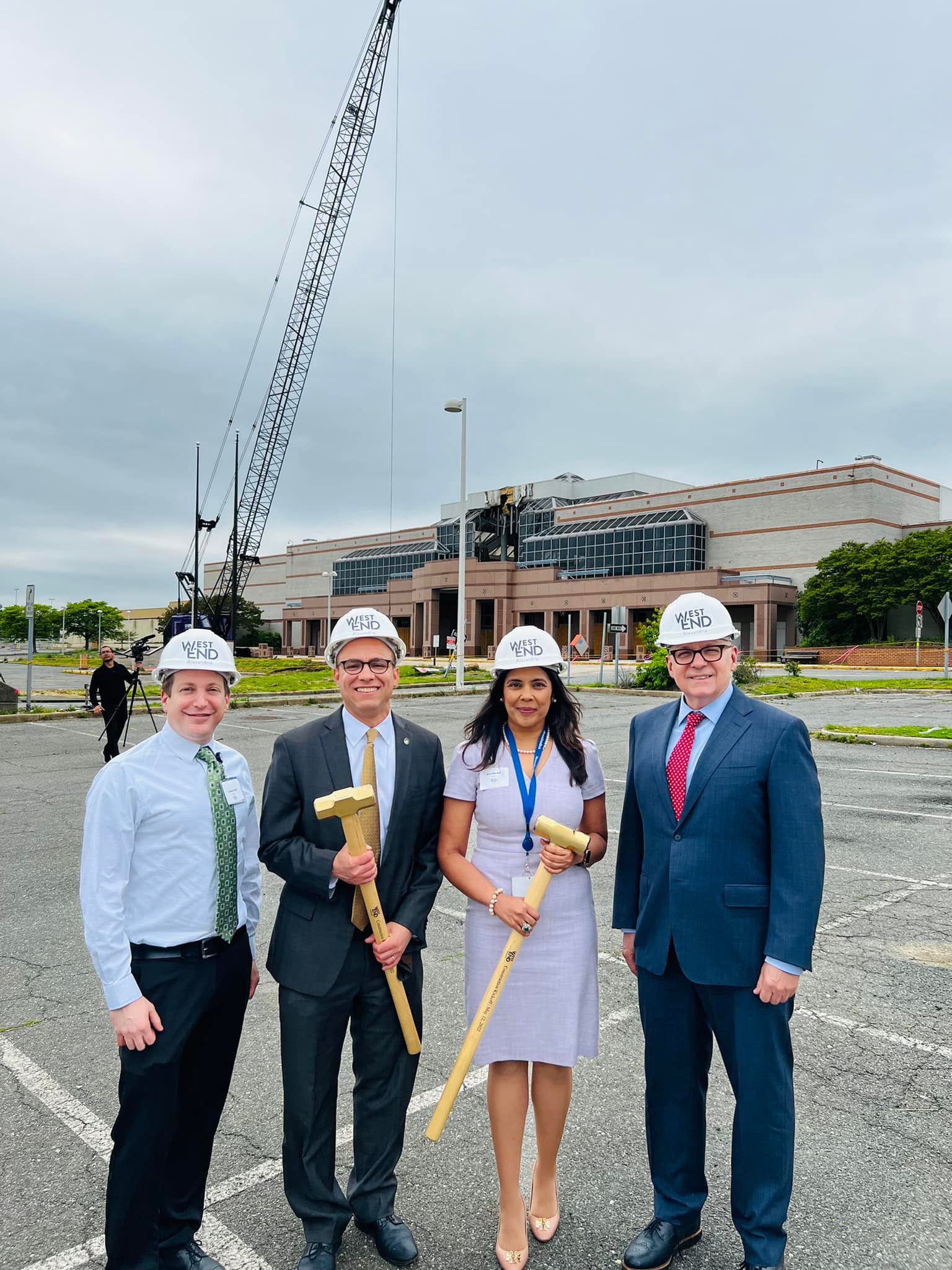 four people from Alexandria City and Inova Alexandria stand with hard hats and hammers in front of landmark mall