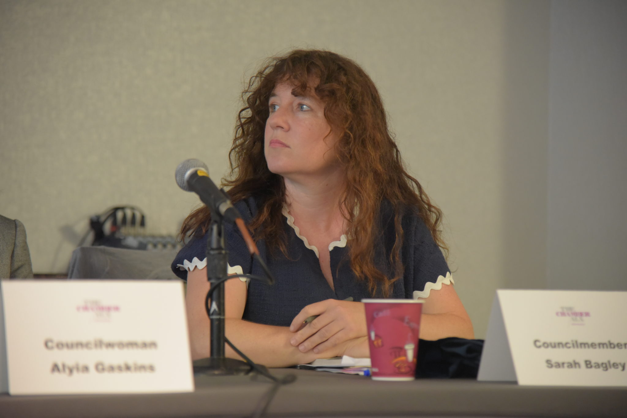 woman sits at table in front of microphone and looks over her right shoulder