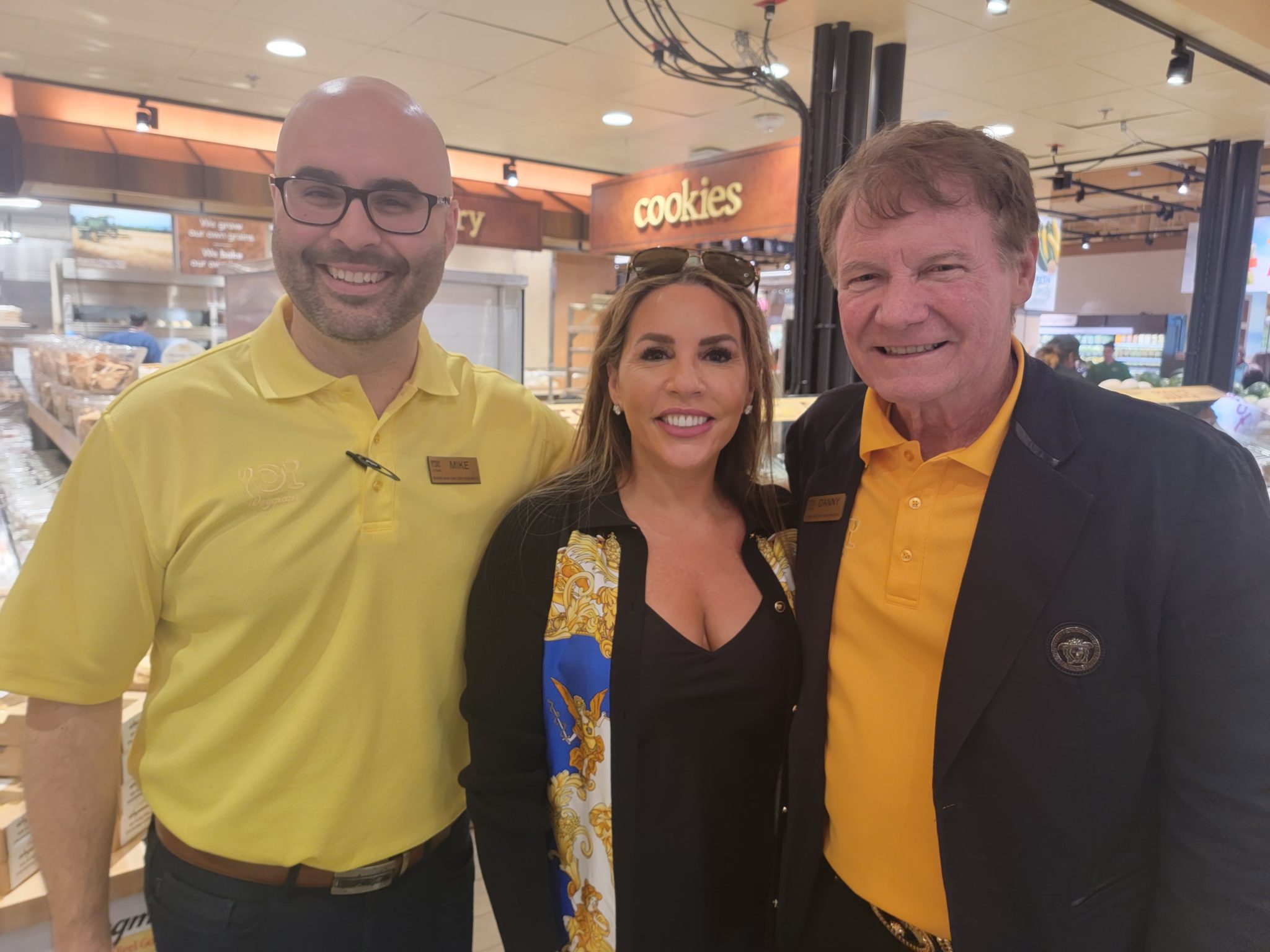 three people in a Wegmans grocery story stand together and smile