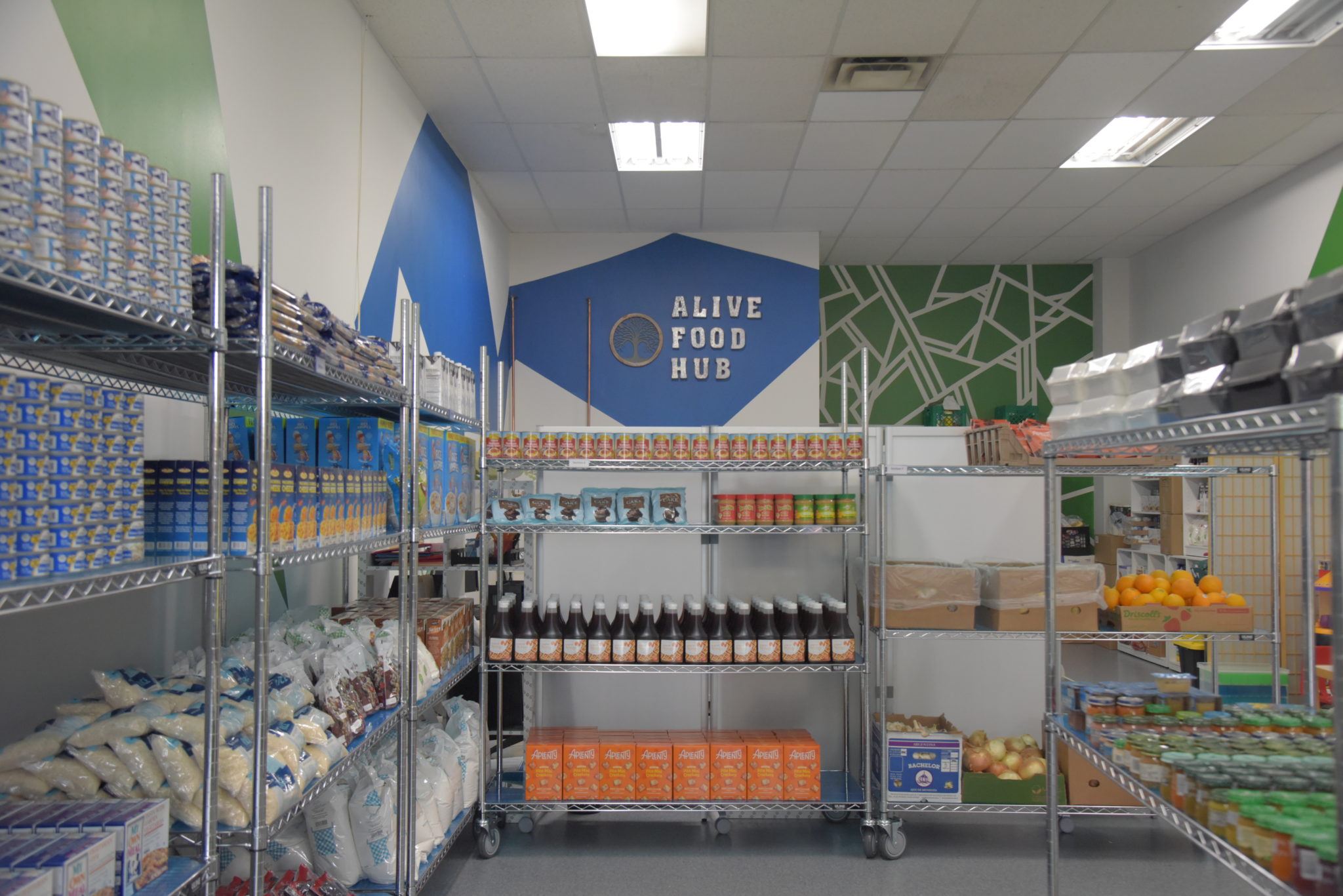 a shelf of canned goods in front of a wall that reads ALIVE FOOD HUB