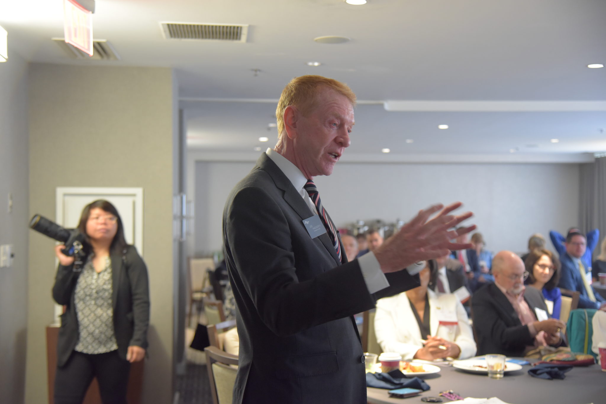 man in suit holds hands out to speak in crowded room 