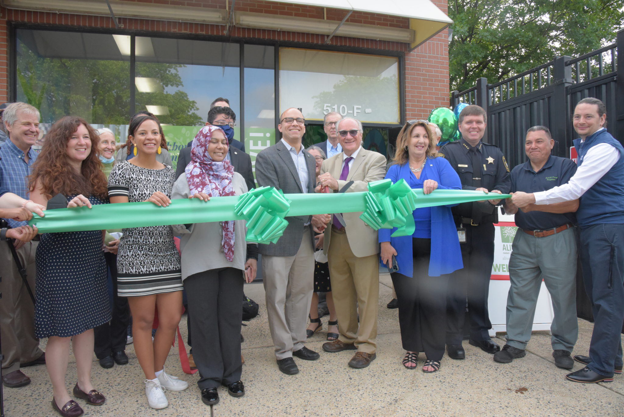 a group of Alexandria city officials including the mayor stand in front of a ribbon with a giant pair of scissors