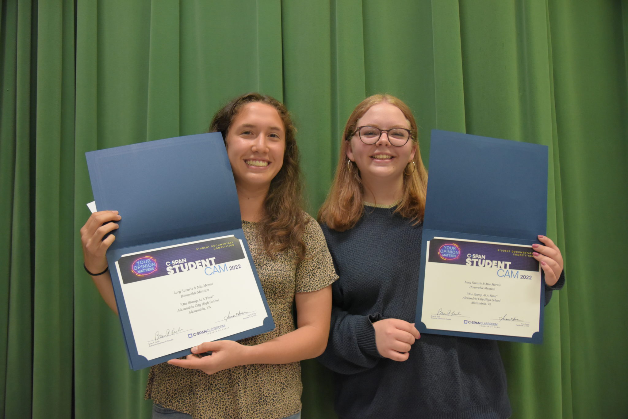 two girls hold up certificates