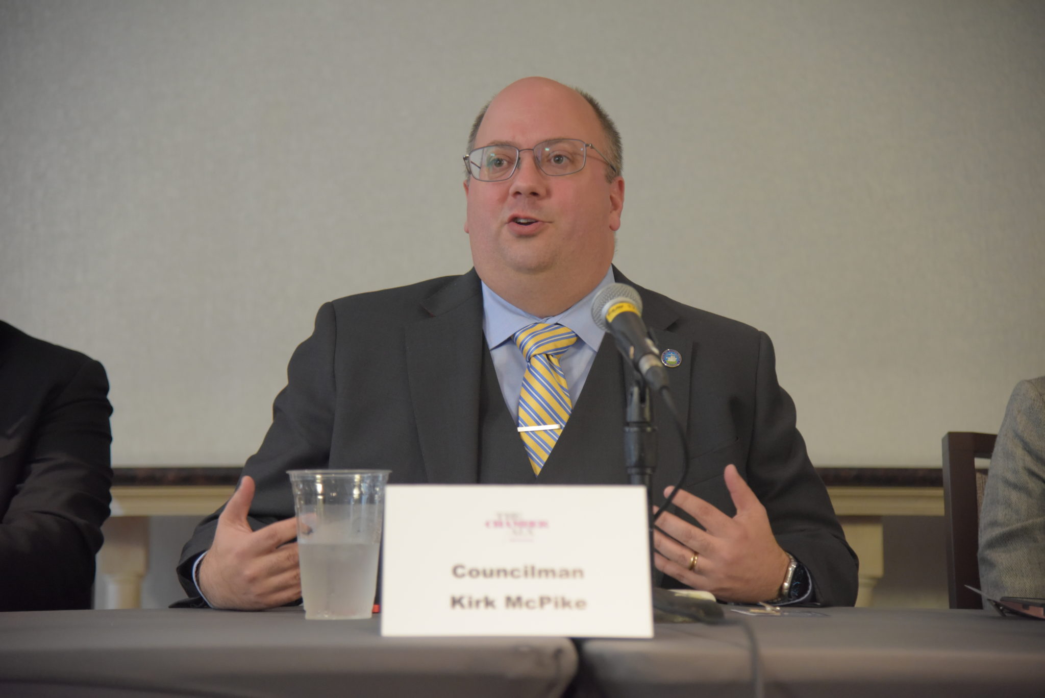 Man in Suit Sits at Table Behind Microphone