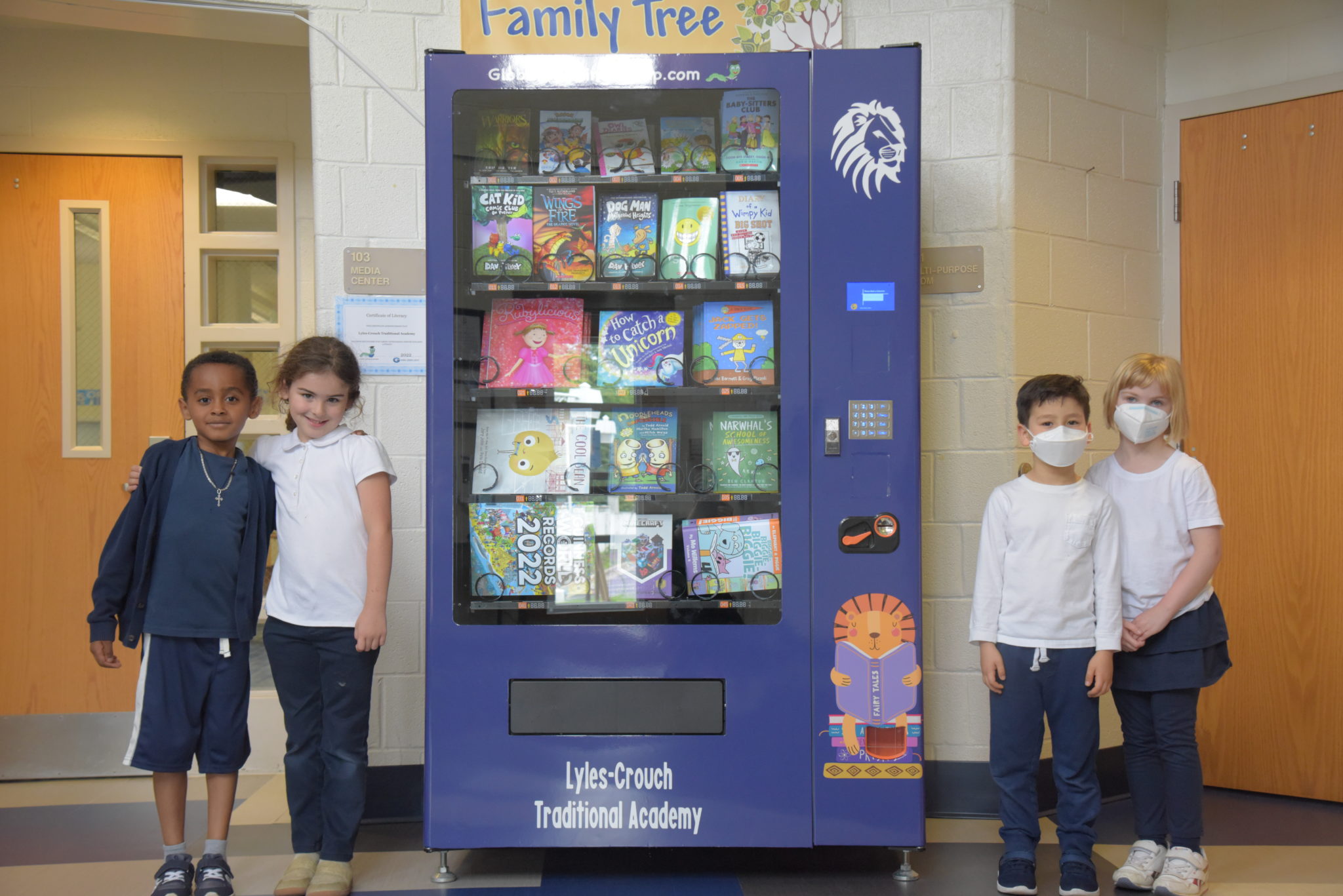 four students - two on each side - stand next to the brand new book vending machine at Lyles-Crouch Traditional Academy