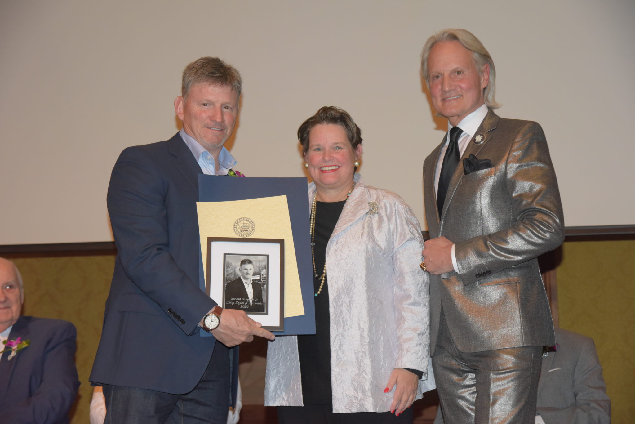 Donald Simpson Jr. holds photo and certificates and stands next to Mary Wadland and Monte Durham