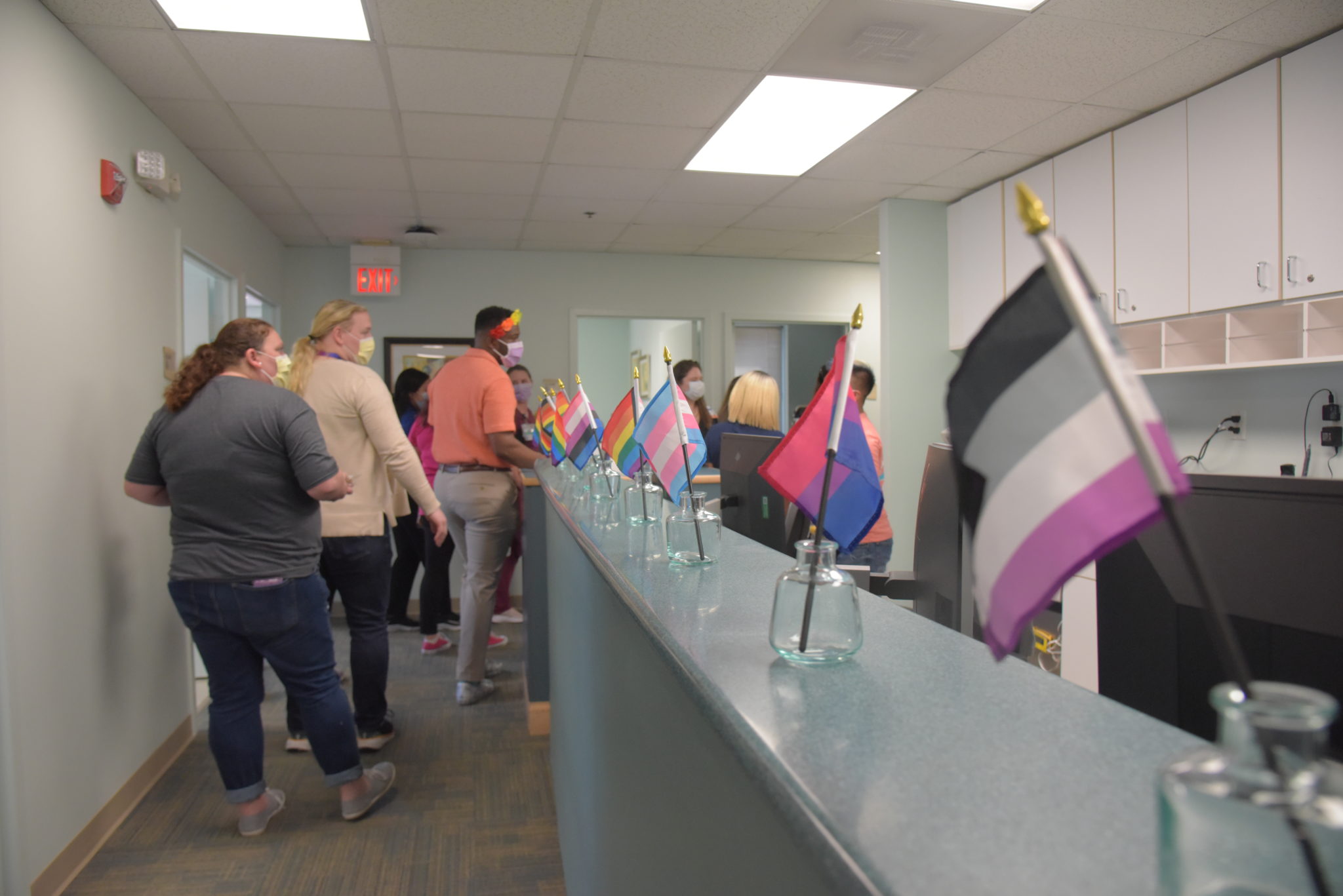 a hallway filled with people in single file line, rainbow pride flags are lined on a counter top in mason jars