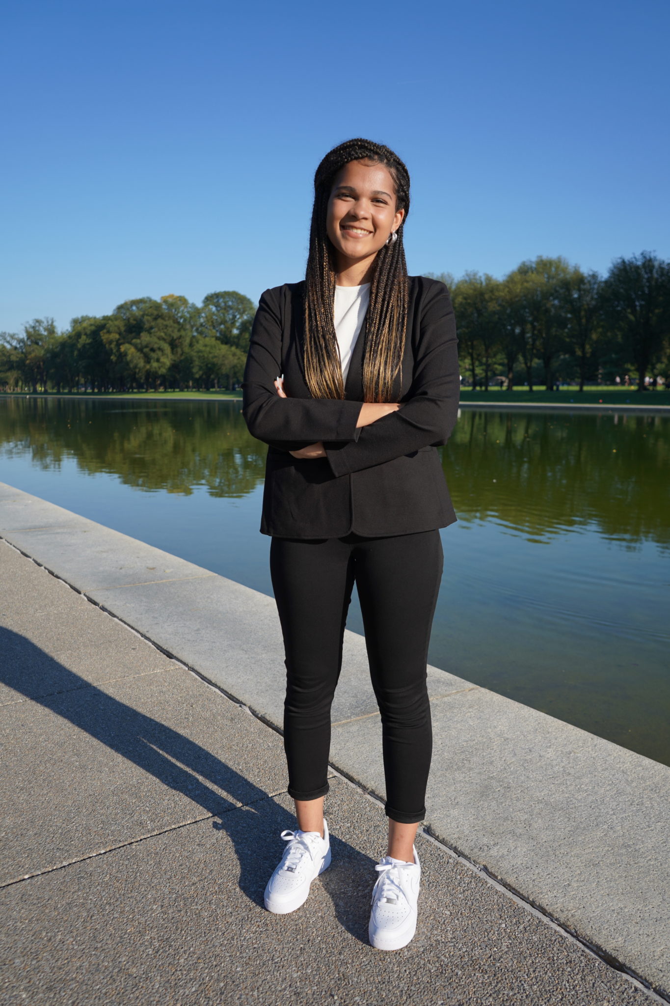 a woman in a pants suit poses with arms crossed and smile in front of the reflection pool in Washington DC