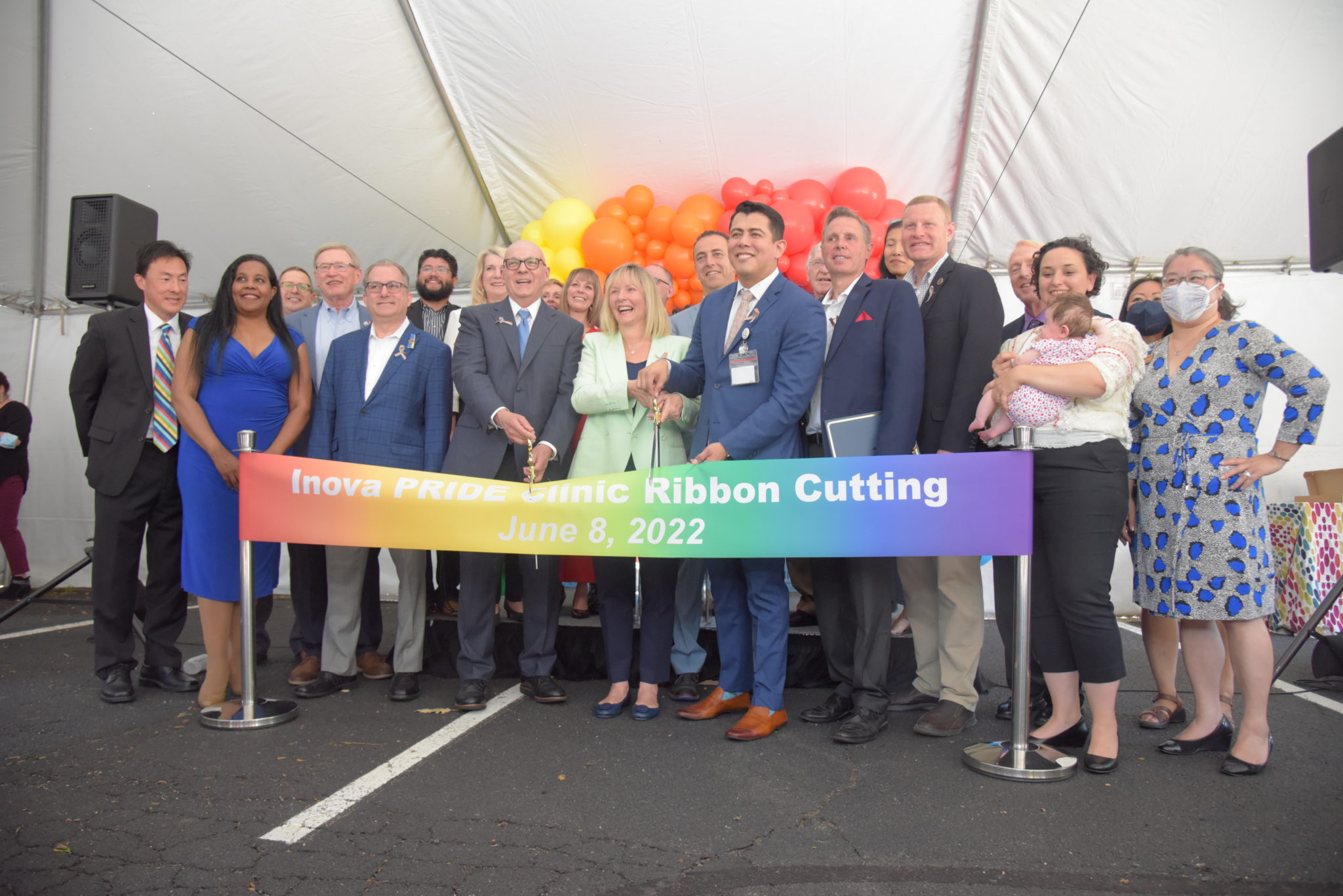 Inova officials cutting the Inova Pride Clinic rainbow ribbon under a tent in the parking lot surrounded by rainbow balloons