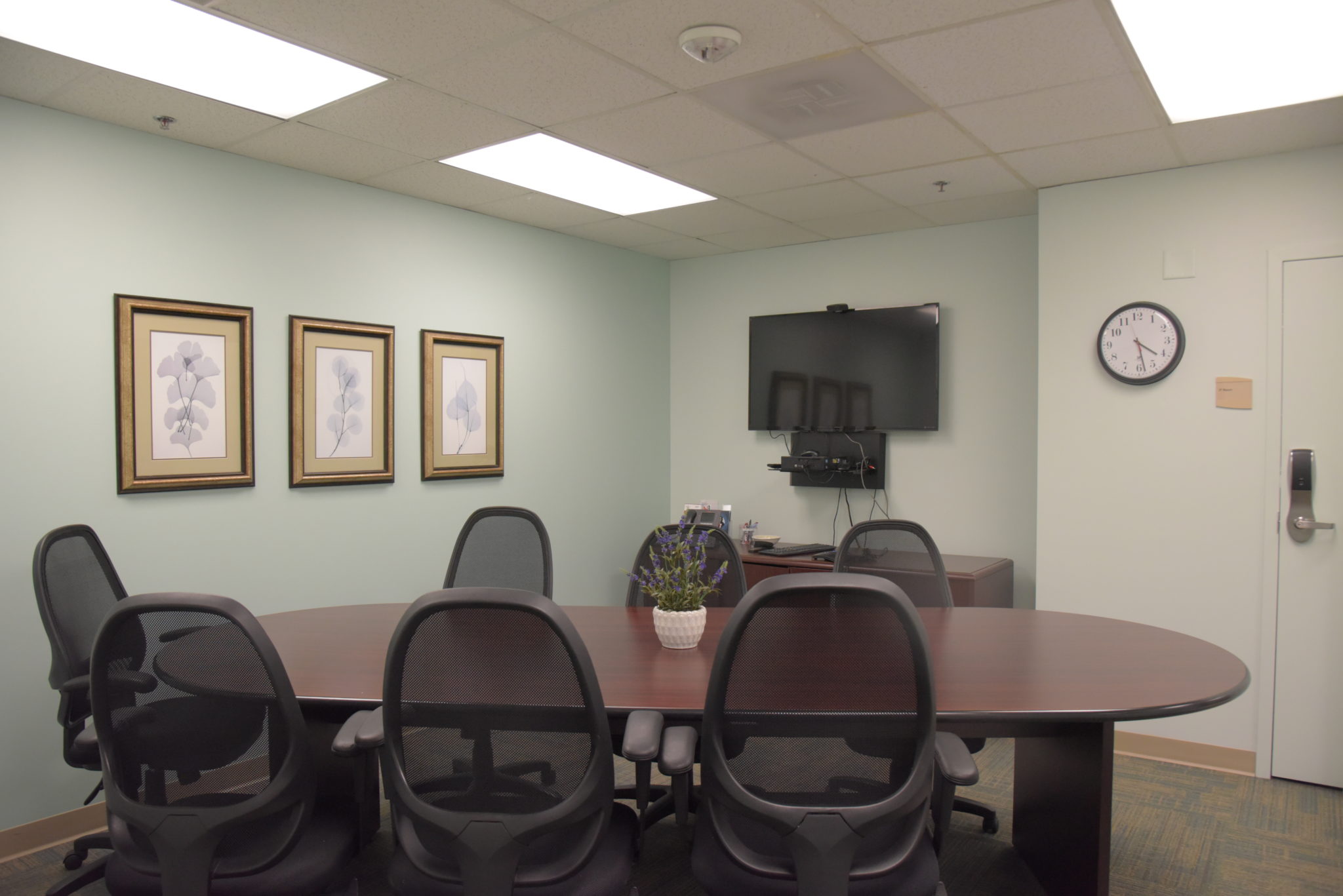 a conference room with an oval table surrounded by six swivel desk chairs