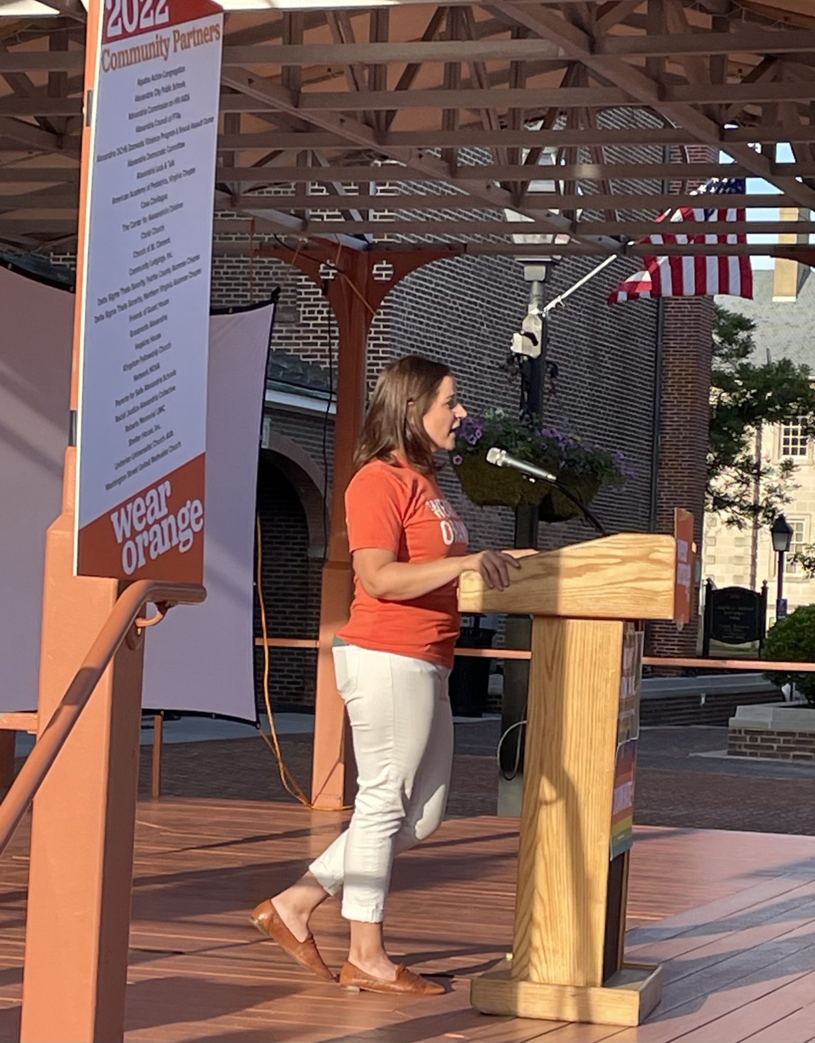 woman in orange t shirt stands at podium reading names of gun violence victims 