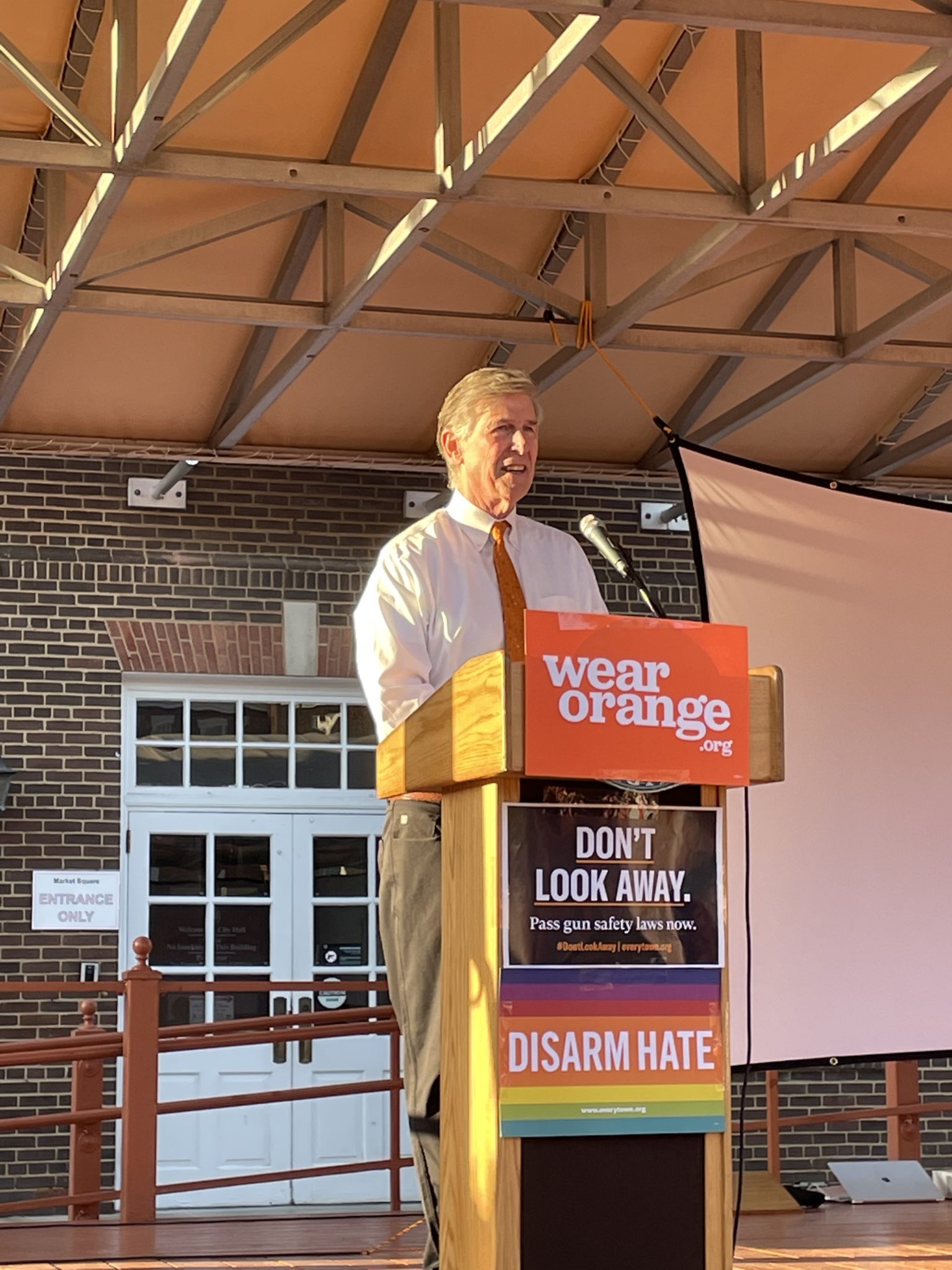 congressman Don Beyer at a podium with a sign which reads "wear orange" for gun violence