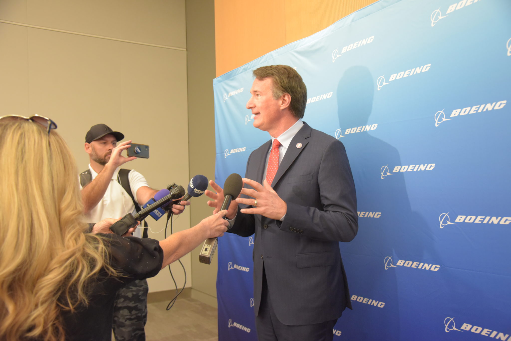 Virginia Governor Glenn Youngkin stands in front of Boeing sheet with cameras and microphones pointed in his face