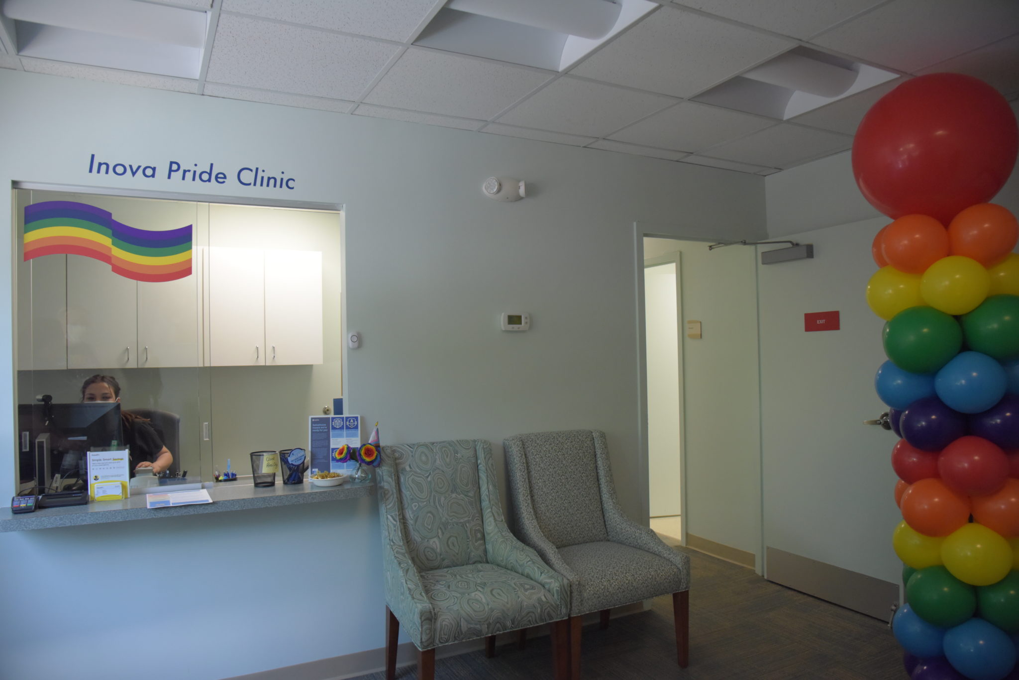 the inova pride clinic waiting room, with reception desk, two chairs, and rainbow flag on the wall