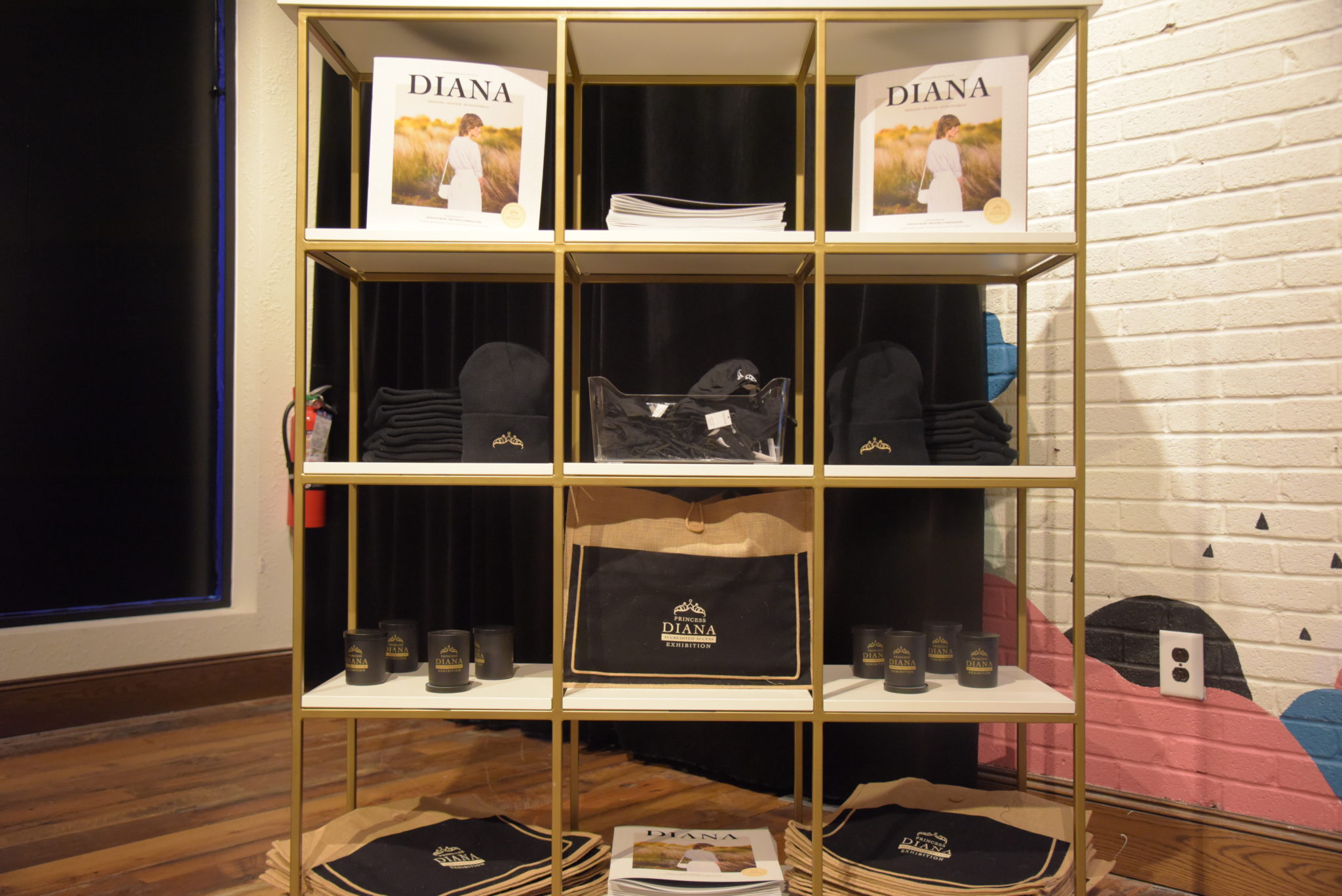 a cubic shelf with two books of princess diana, several diana tote bags, and candles and hats with princess diana logo on them