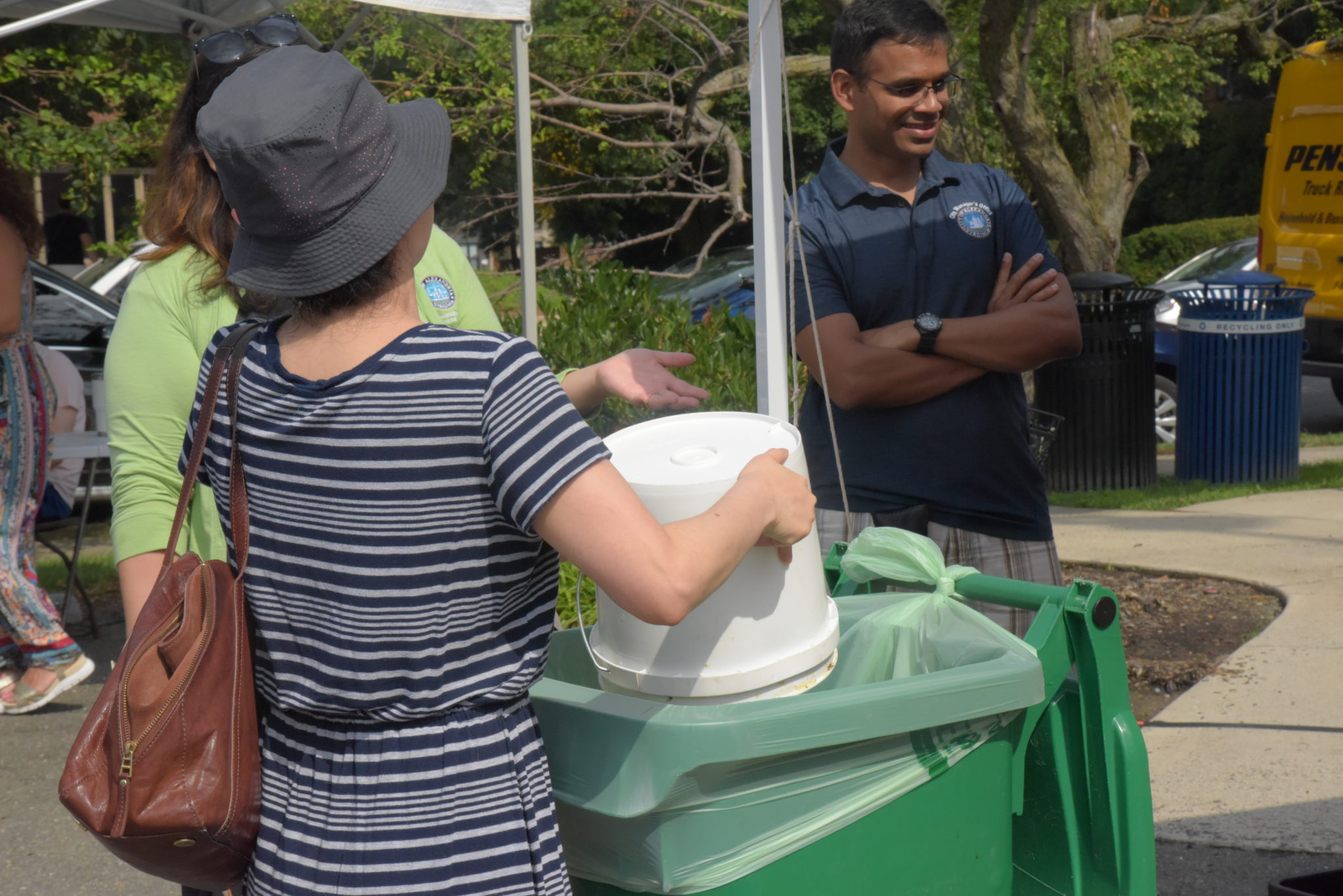 a woman dumps a personal size bin of compost into the new larger compost station at Old Town North Farmers Market 