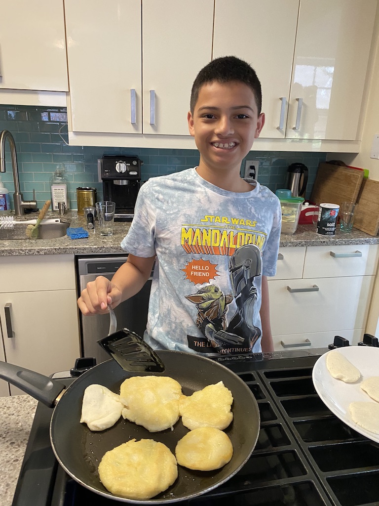 a young boy smiles at the camera as he cooks cakes in a pan