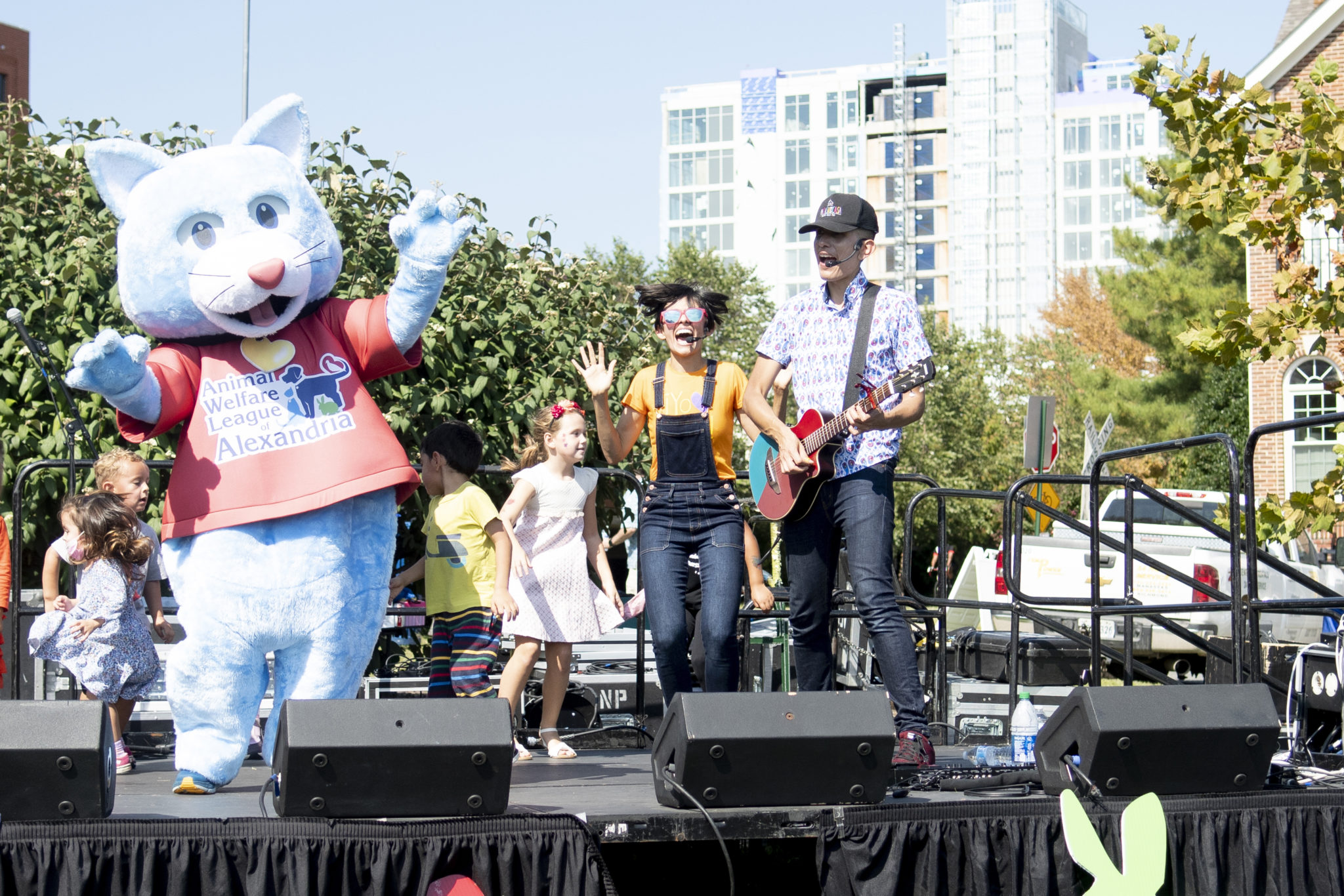 a group of people with a person in a large cat mascot costume dance and sing on a stage