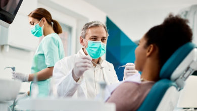 a dentist holds a hand mirror up to a patient in a chair