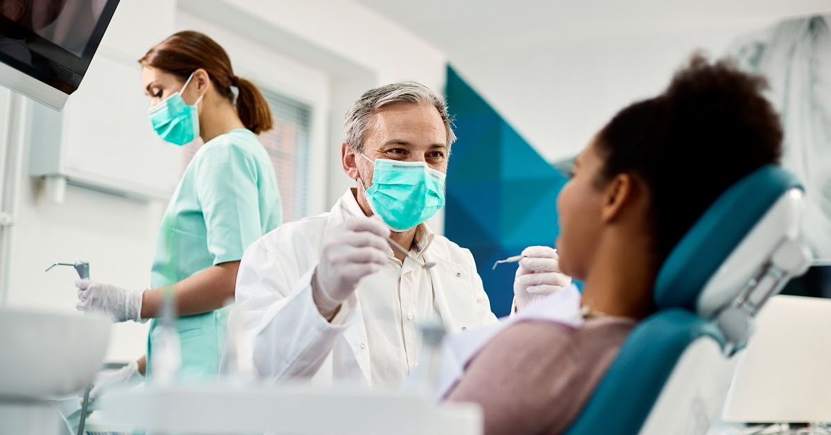 a dentist holds a hand mirror up to a patient in a chair